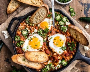 eggs in a skillet with toasted garlic bread and jalapenos