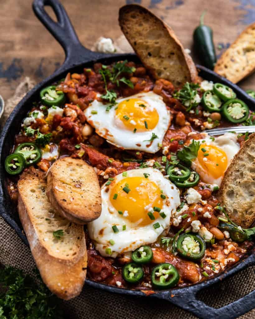 spicy white bean shakshuka with eggs and toasted garlic bread in the skillet