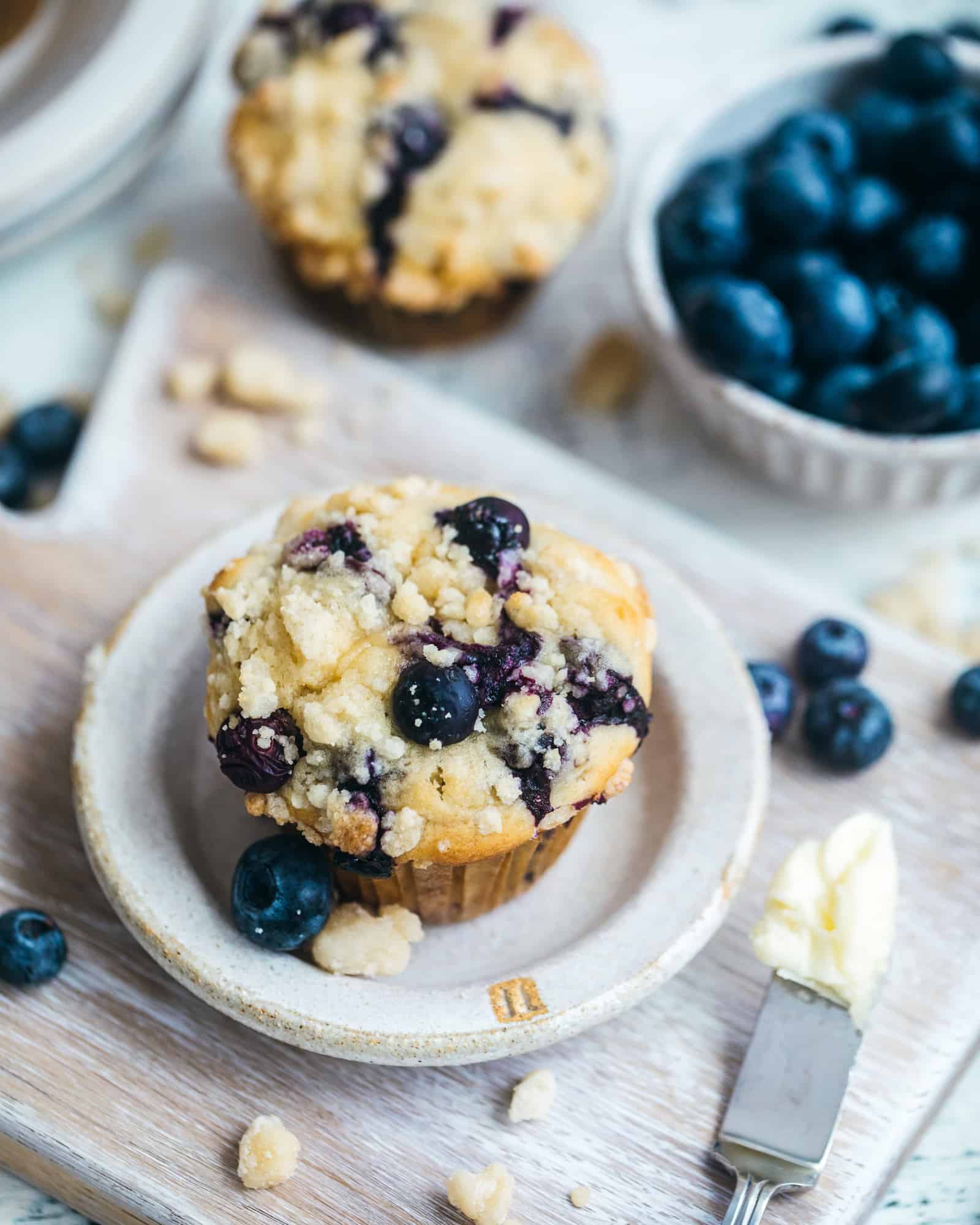 blueberry crumb cake muffins on a plate with a bowl of blueberries