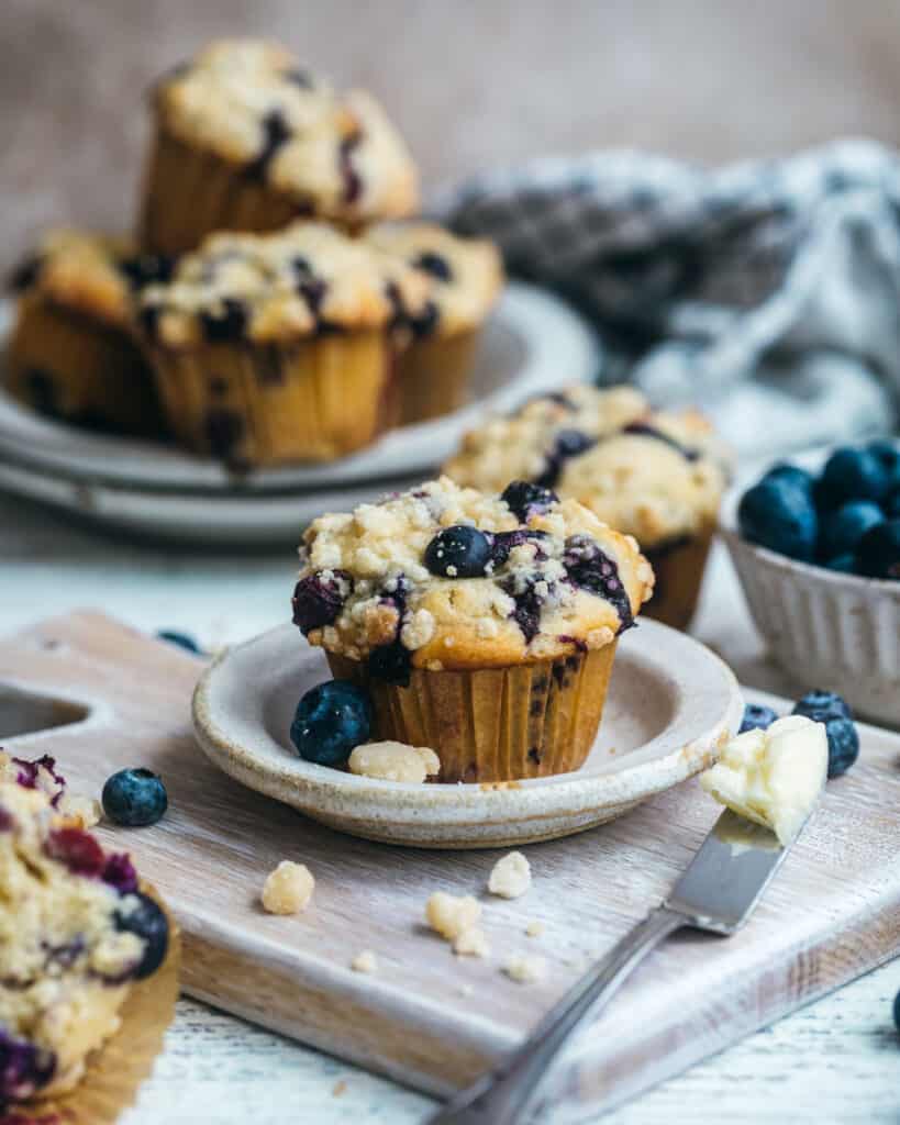 blueberry crumb cake muffins on a cutting board with a buttered knife