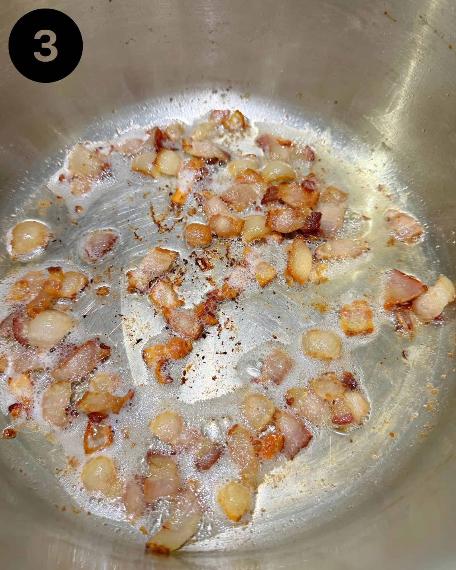 chunks of bacon being rendered in a large dutch oven.