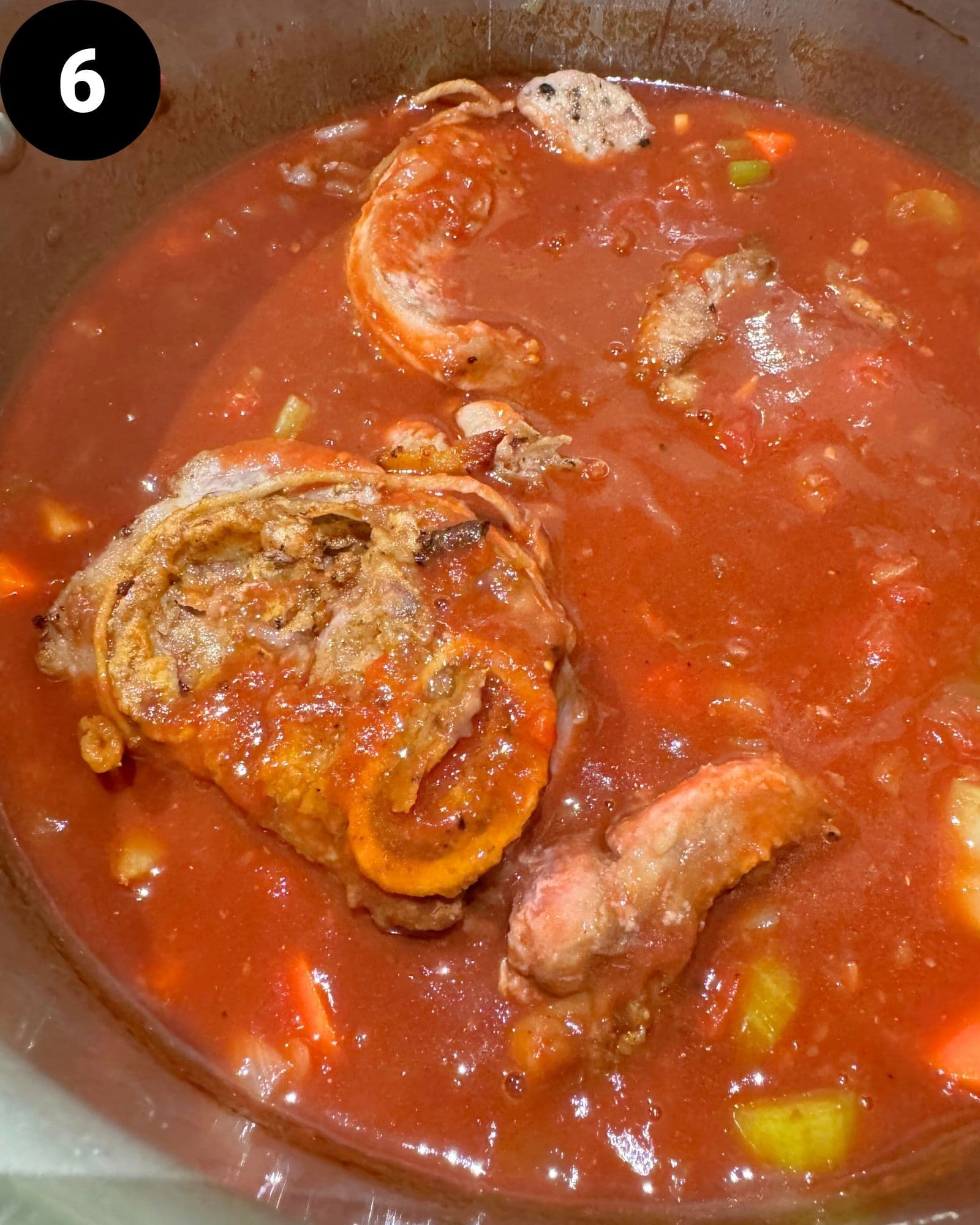 beef osso buco in a large pot covered in tomato sauce and vegetables.