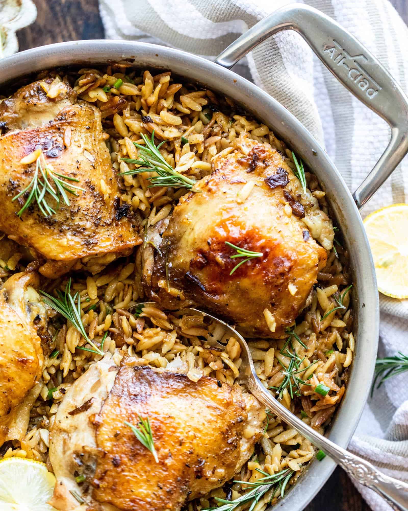 rosemary chicken with parmesan orzo in a pan with a spoon and lemons