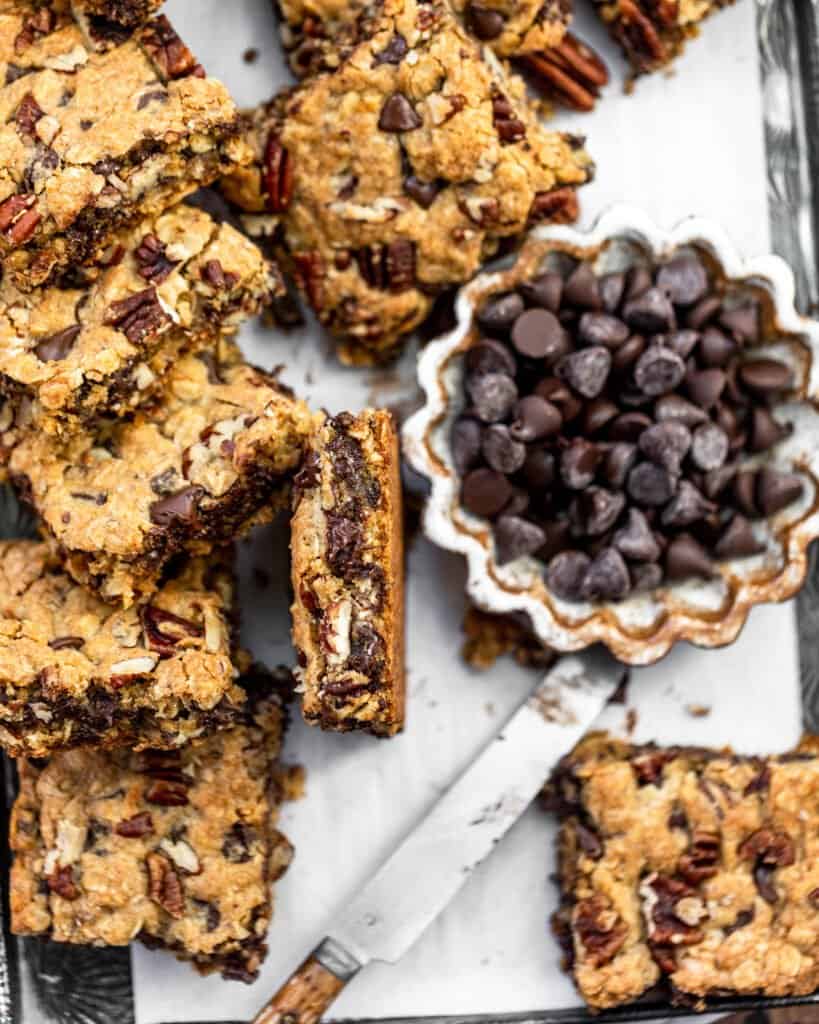 cut up chocolate chip pecan oatmeal bars on a baking sheet with a bowl of chocolate chips