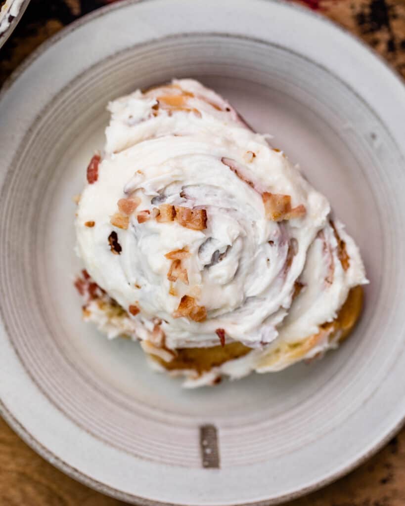 a cinnamon roll on a plate with icing and bacon on top
