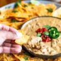 a hand dipping a tortilla chip into the chunky vegan queso dip