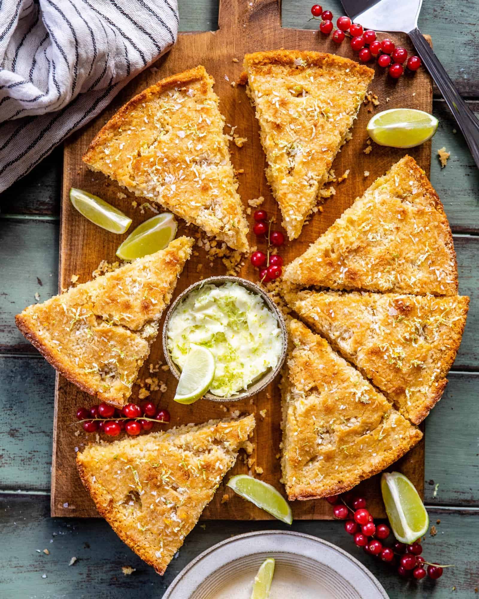 Coconut Cornbread sliced on a serving board with sweet lime butter and red currants