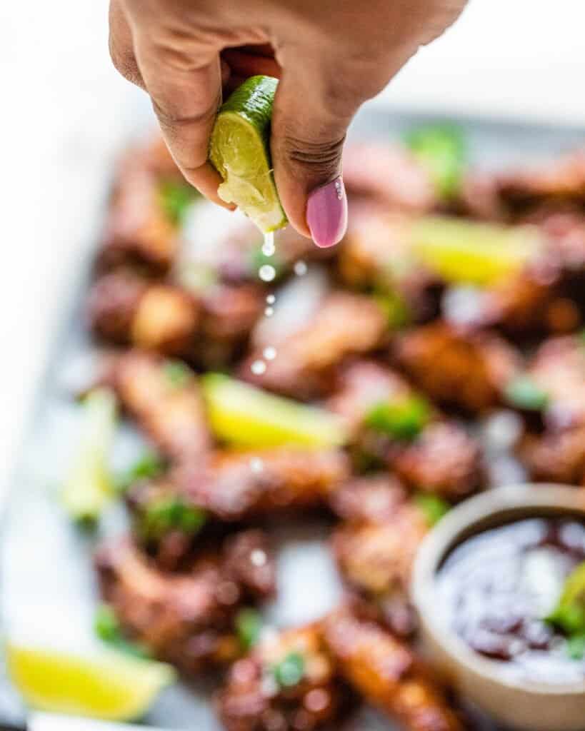 a hand squeezing a lime on top of the cajun bbq wings
