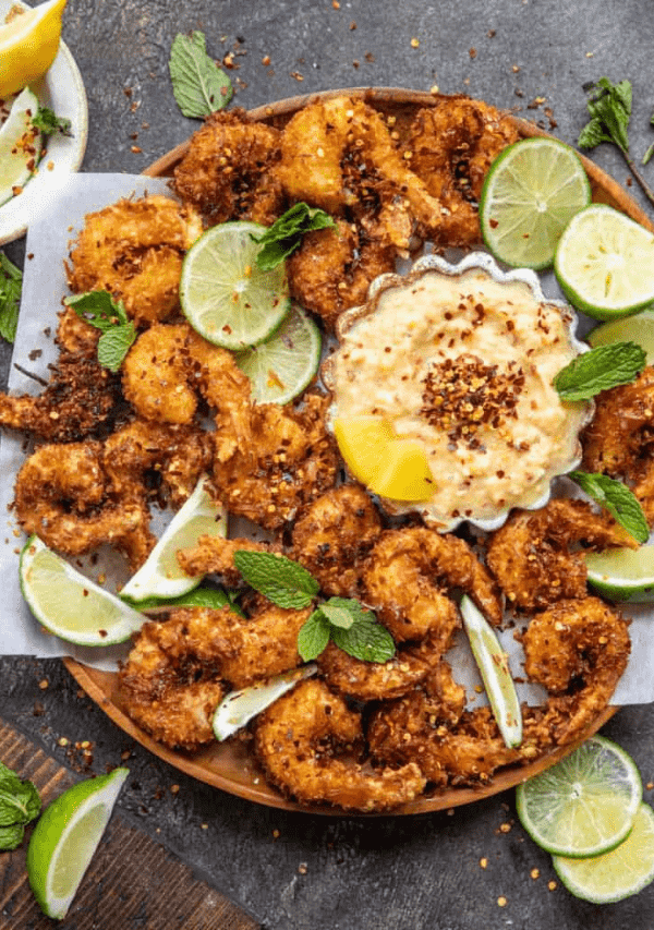 fried shrimp on a serving tray with limes and dipping sauce