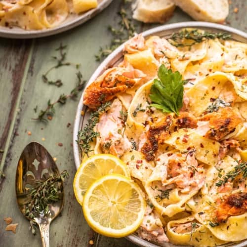 salmon pasta on a plate with lemon and a spoon next to the plate with fresh thyme