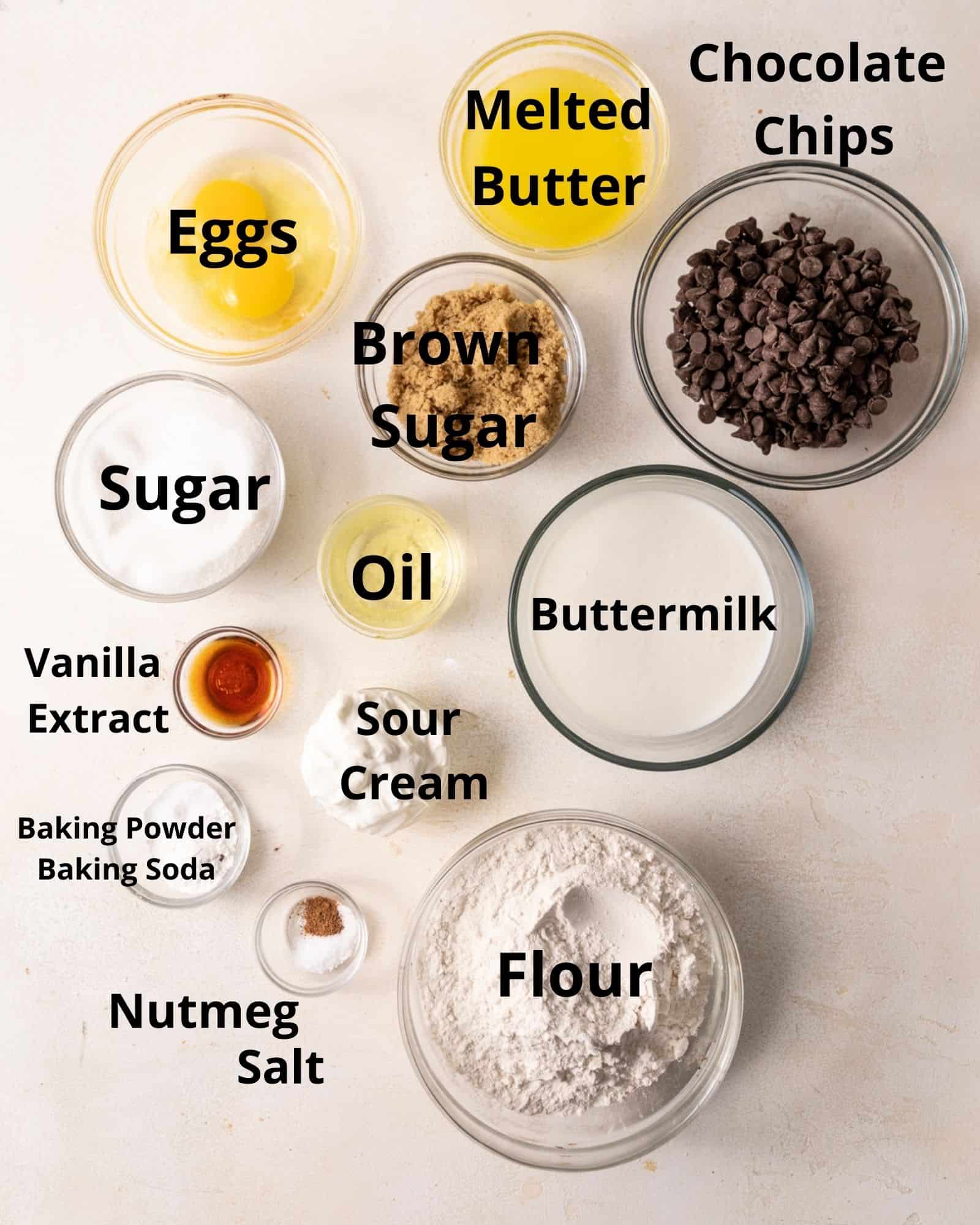 ingredients to make chocolate chip muffins - eggs, sugar, melted butter, brown sugar, sugar, oil, vanilla extract, sour cream, buttermilk, flour, baking powder, baking soda, salt, nutmeg, and chocolate chips.