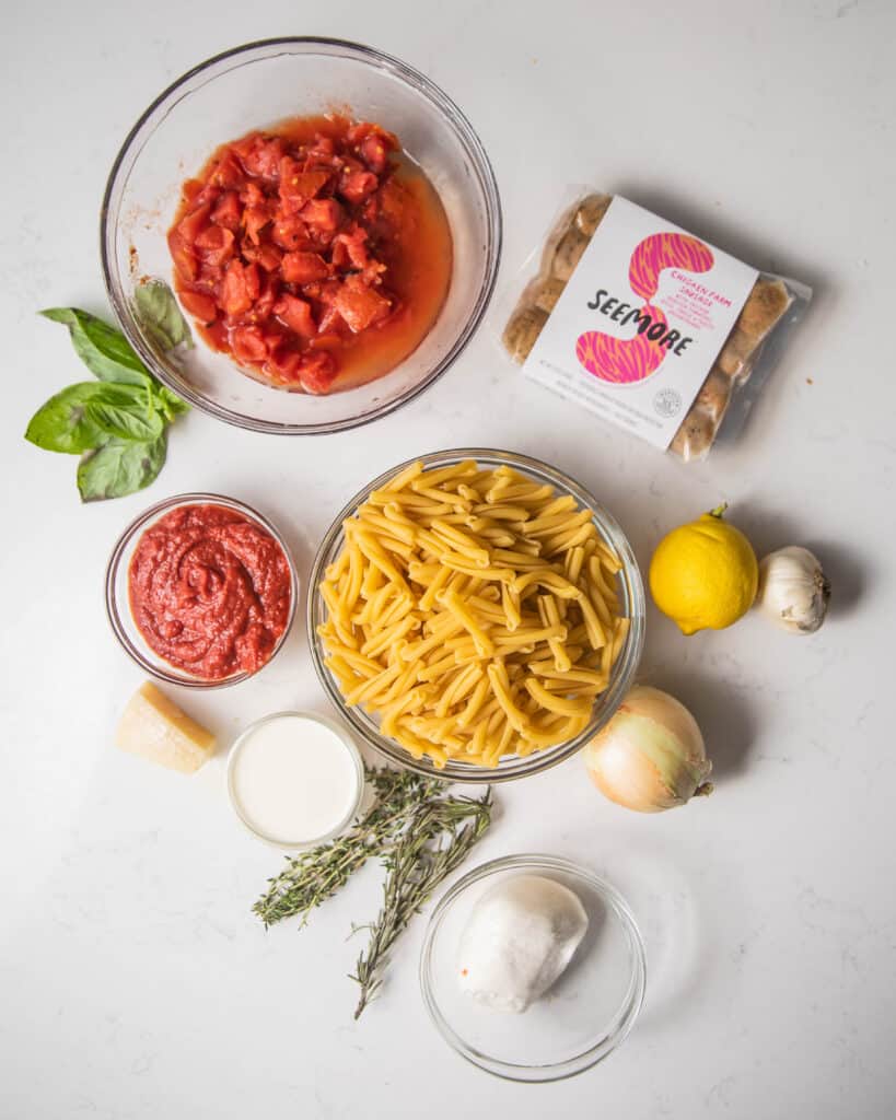 ingredients for cassarecce pasta - crushed tomatoes, sausages, pasta, onion, garlic, basil, tomato paste, herbs, and parmesan