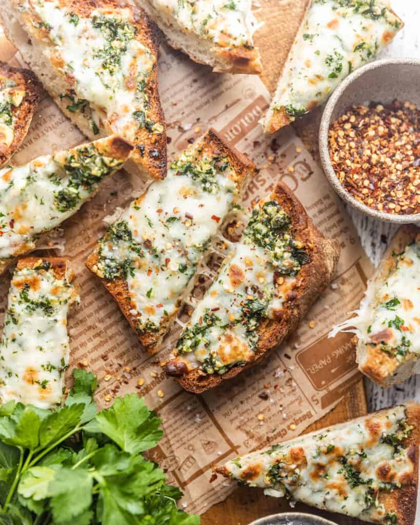cheesy garlic bread with a bowl of red pepper flakes and parsley