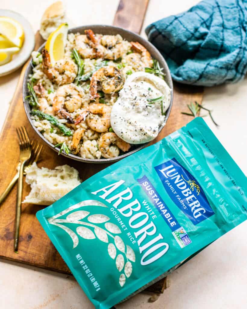 a package of lundberg farms arborio rice on a serving board with a bowl of risotto