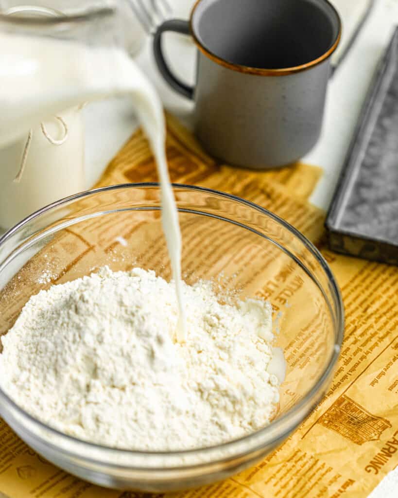 pouring buttermilk into a mixing bowl filled with flour