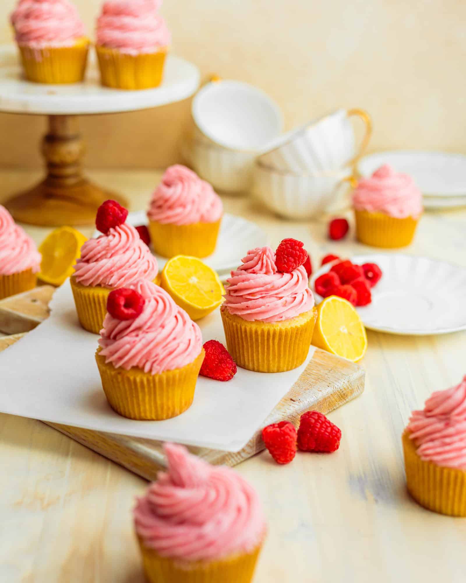 lemon raspberry cupcakes on a serving board with fresh raspberries and lemon slices
