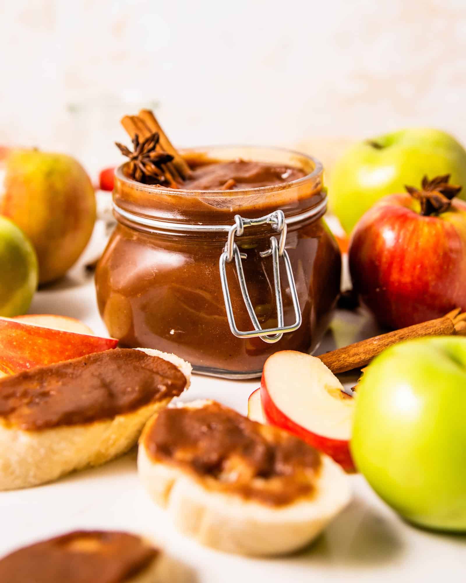 homemade apple butter in a jar surrounded by apples and toast