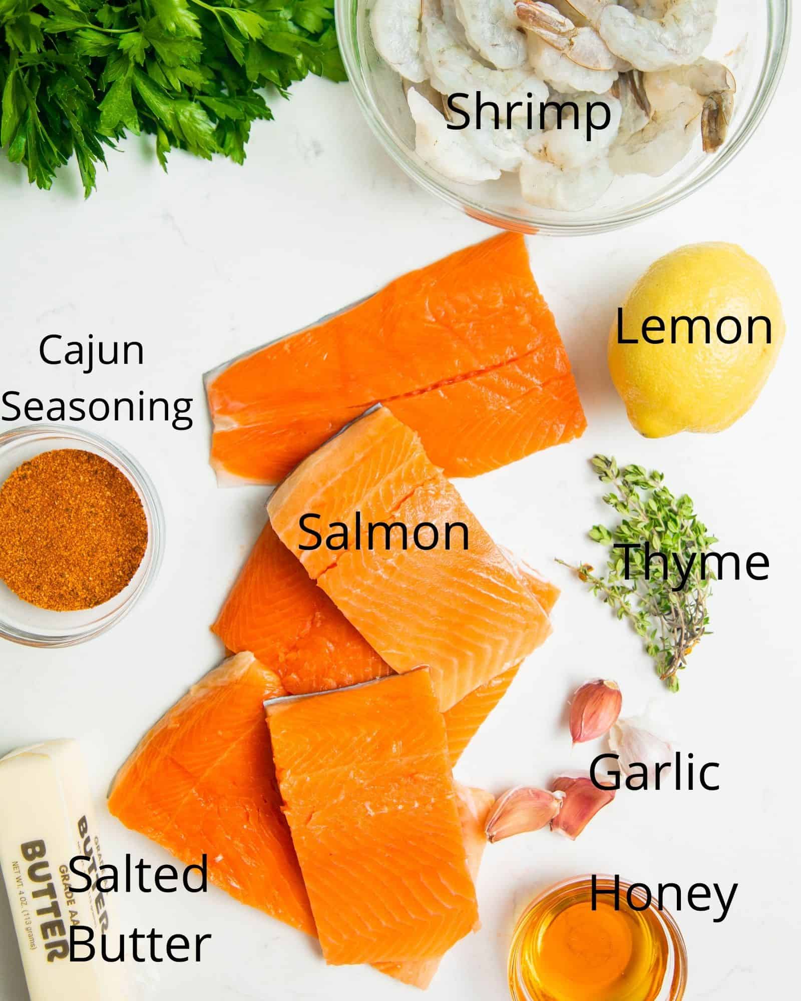 the ingredients needed to make salmon new orleans on a white surface - salmon filets, lemon, shrimp, cajun seasoning, honey, garlic, thyme, and butter