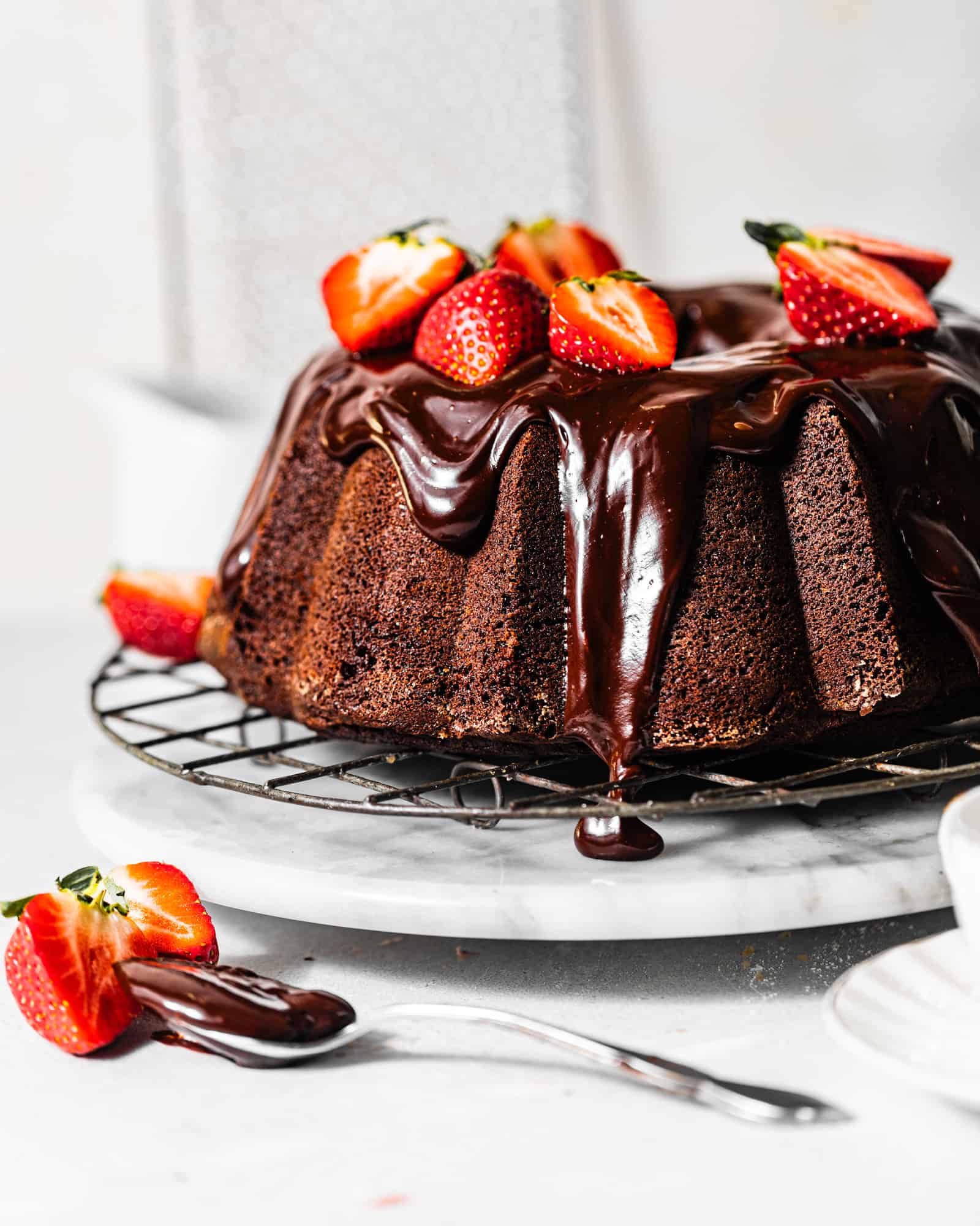 chocolate pound cake with chocolate ganache on a wire rack topped with strawberries