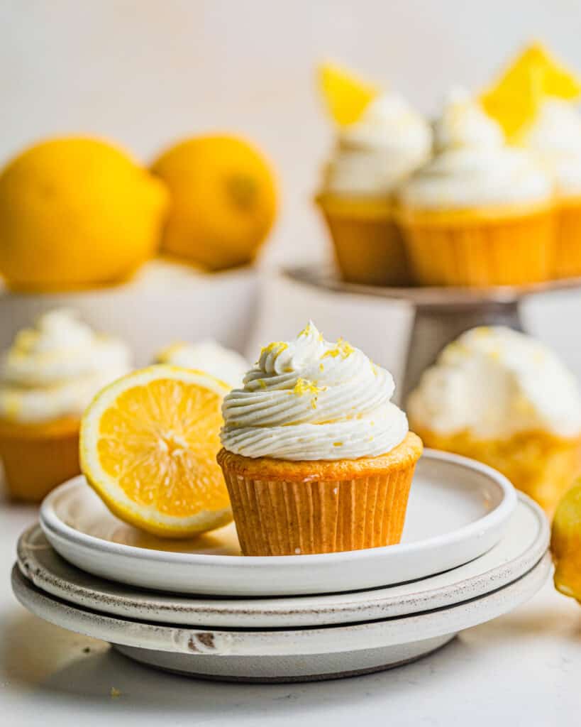 a lemon drizzle cupcake on a plate with more cupcakes behind it.
