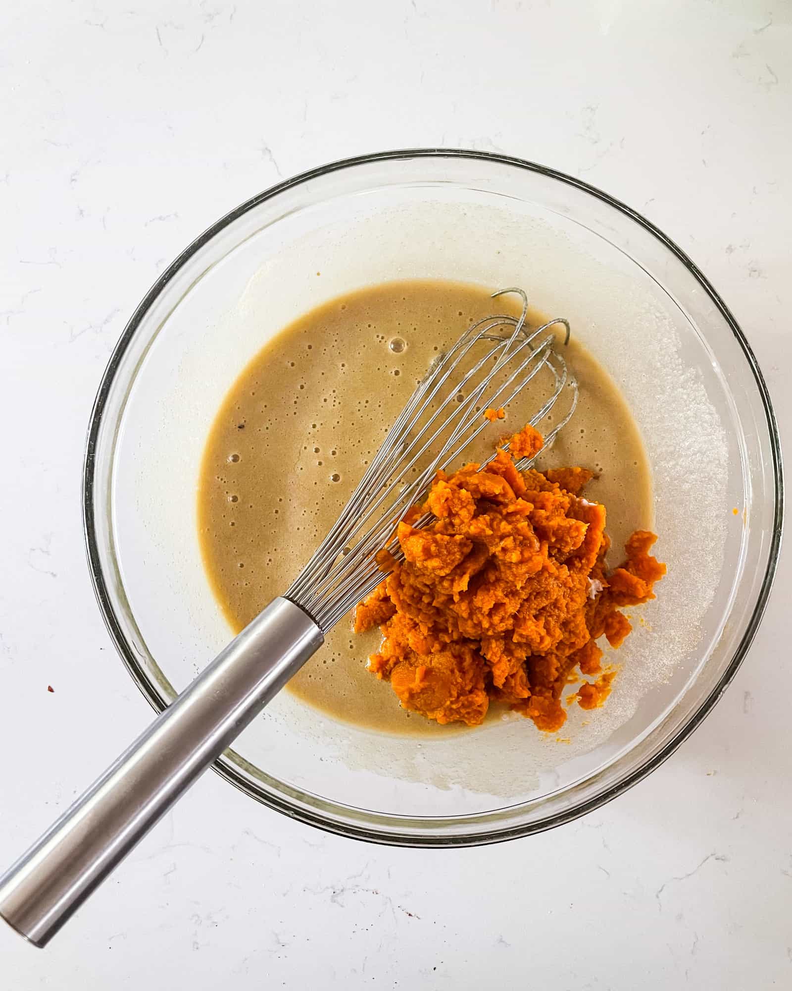 wet ingredients with pureed pumpkin in a bowl with a whisk