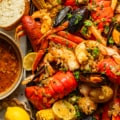 cajun seafood boil recipe on a large serving tray next to a bowl of seafood boil sauce, bread, and sliced lemons