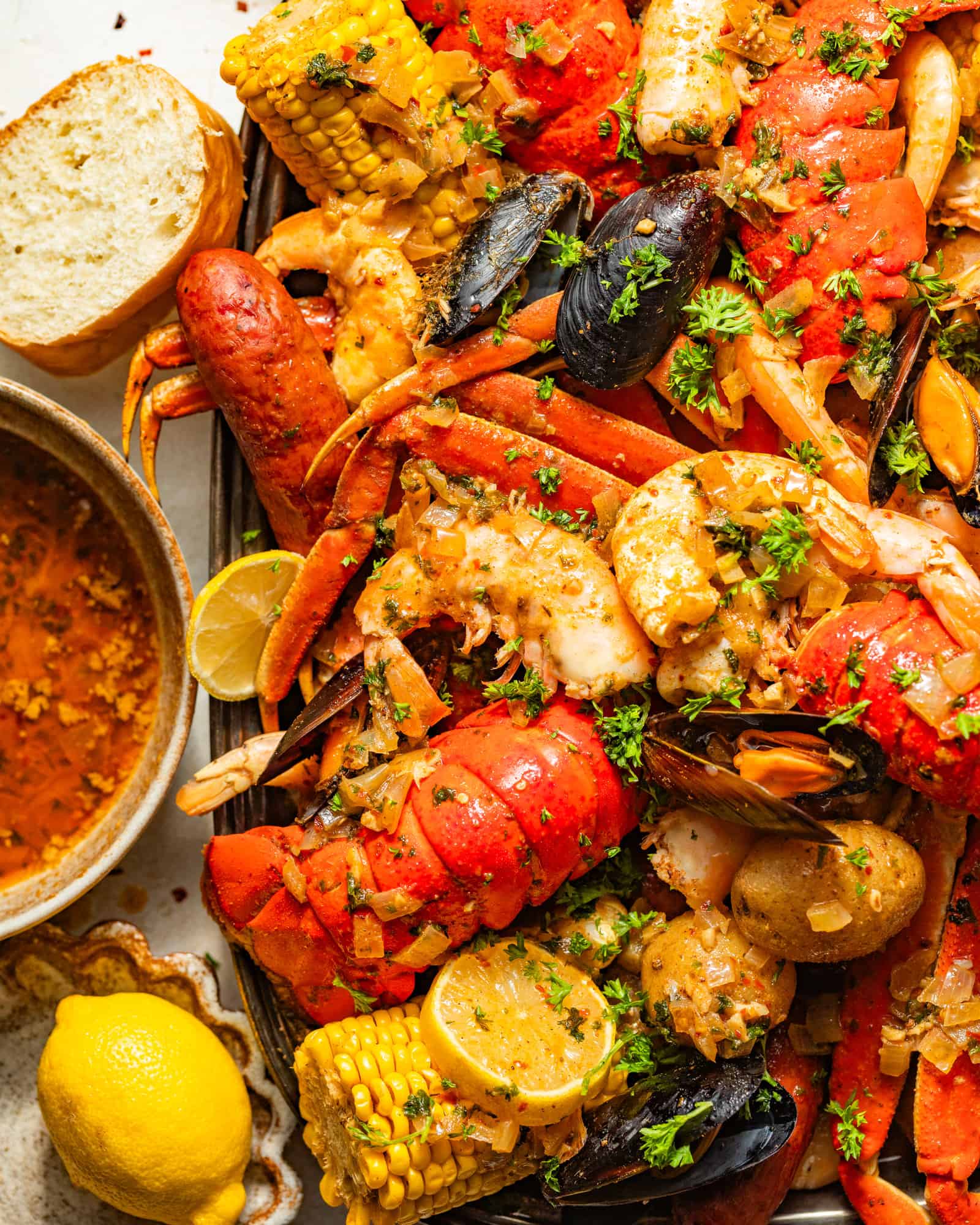 cajun seafood boil recipe on a large serving tray next to a bowl of seafood boil sauce, bread, and sliced lemons