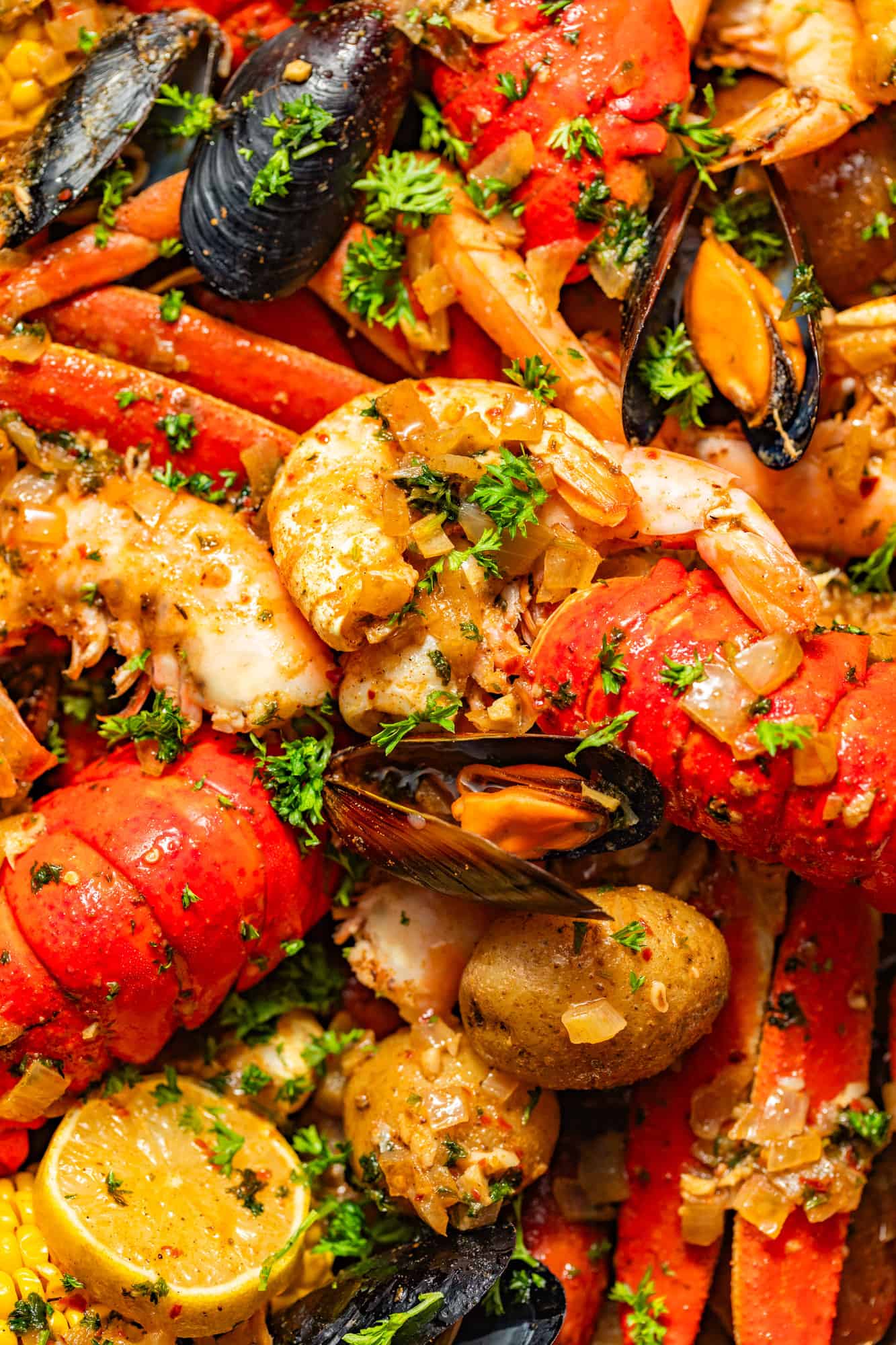 up close photo of shrimp, lobsters, mussels, clams, and lemons garnished with parsley and seafood boil sauce