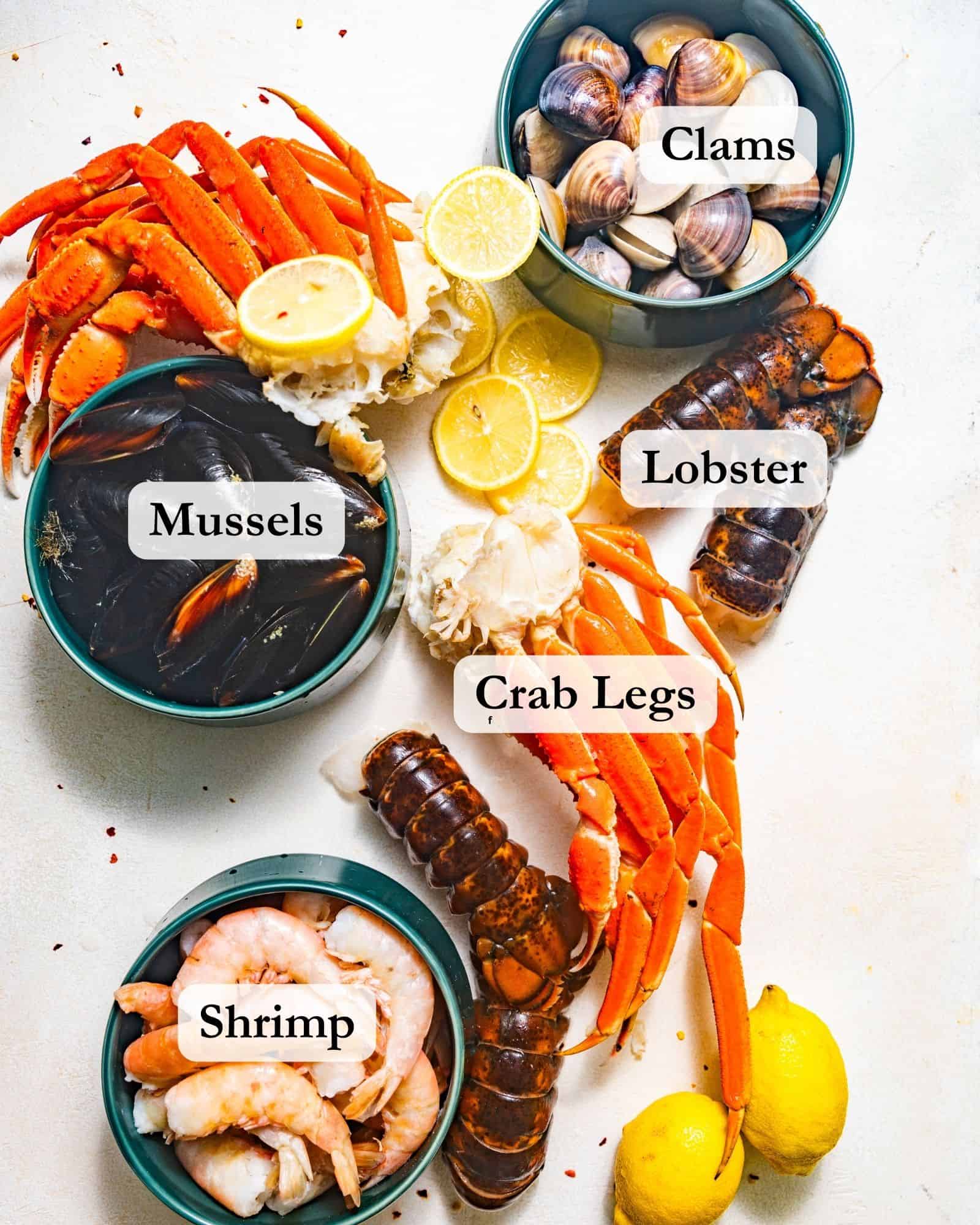 ingredients to make a cajun seafood boil on a white surface - shrimp, lobster, crab legs, mussels, and clams.