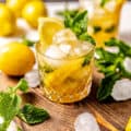 a bourbon smash on a brown serving tray with ice cubes, fresh mint, and sliced lemons.