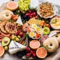 a breakfast charcuterie board filled with bagels, waffles, fresh fruit, cheeses, and cured meats.