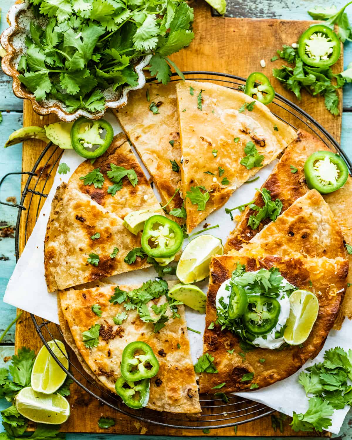 cheese quesadilla on a cooling rack garnished with sliced jalapeños, cilantro, and limes.
