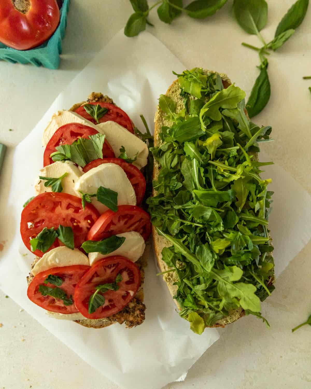 sandwich cut in half with arugula on side and tomatoes fresh mozzarella, and basil on the other.