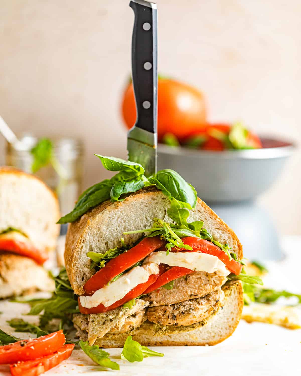 a sliced chicken caprese sandwich in front of a bowl of tomatoes.