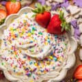 dunkaroo dip in a bowl garnished with rainbow sprinkles and strawberries.