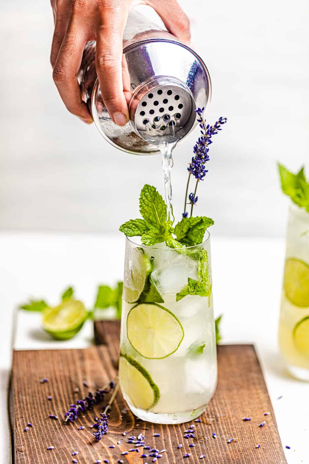 a hand pouring a gin mojito into a highball glass from a cocktail shaker.
