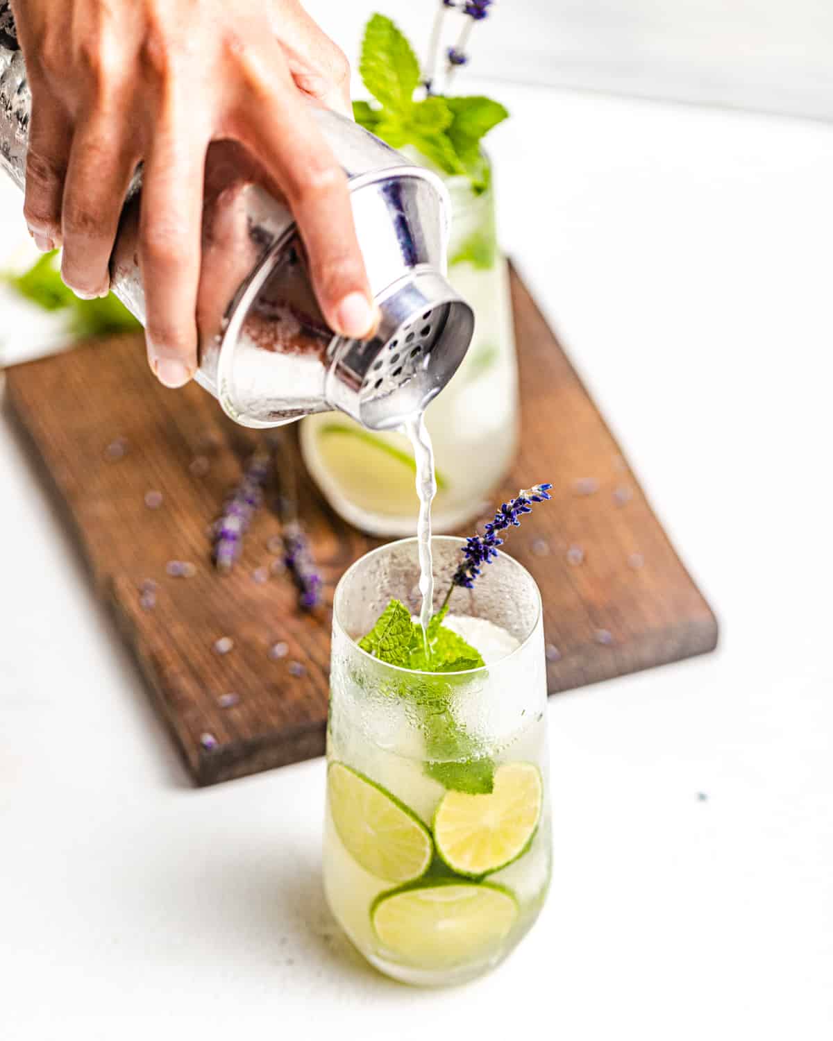 a hand pouring a gin mojito into a highball glass from a cocktail shaker.