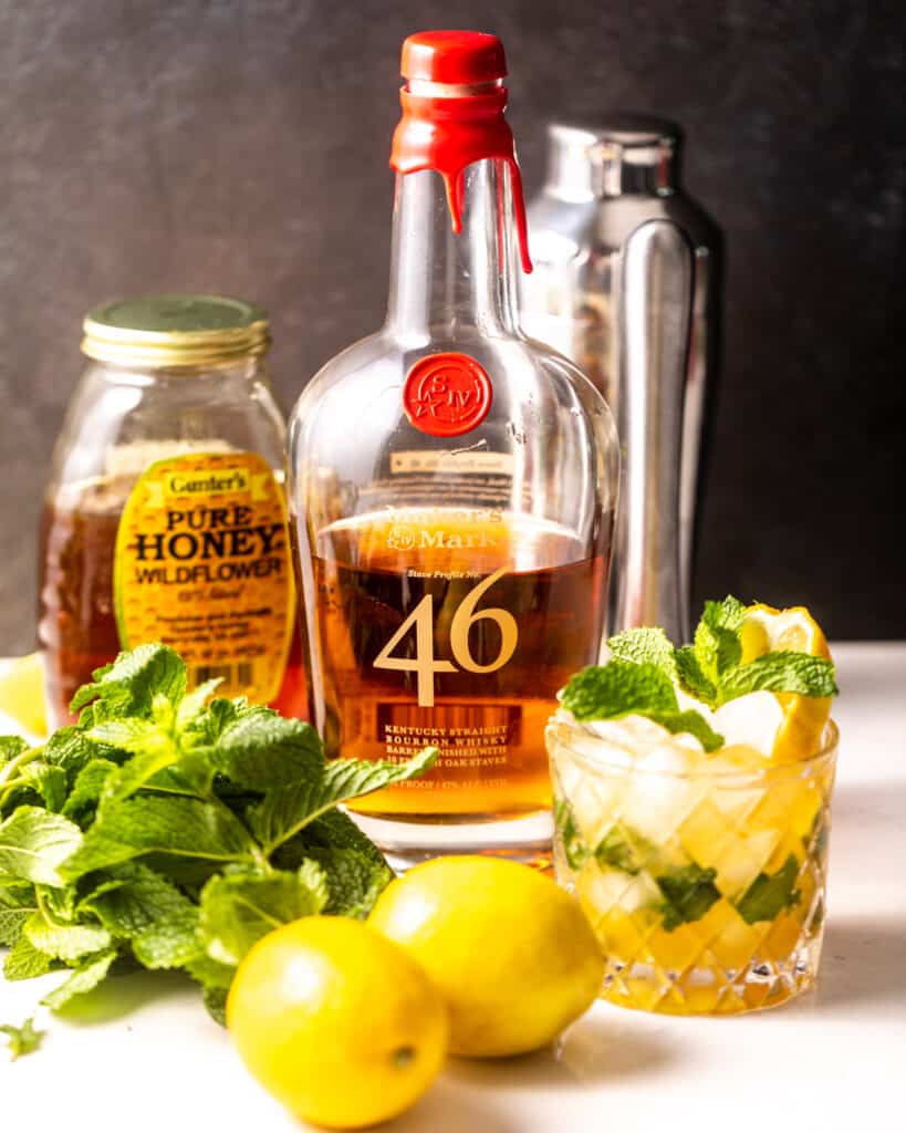 ingredients needed to make a bourbon smash - lemons, whiskey bourbon, mint leaves, and honey.