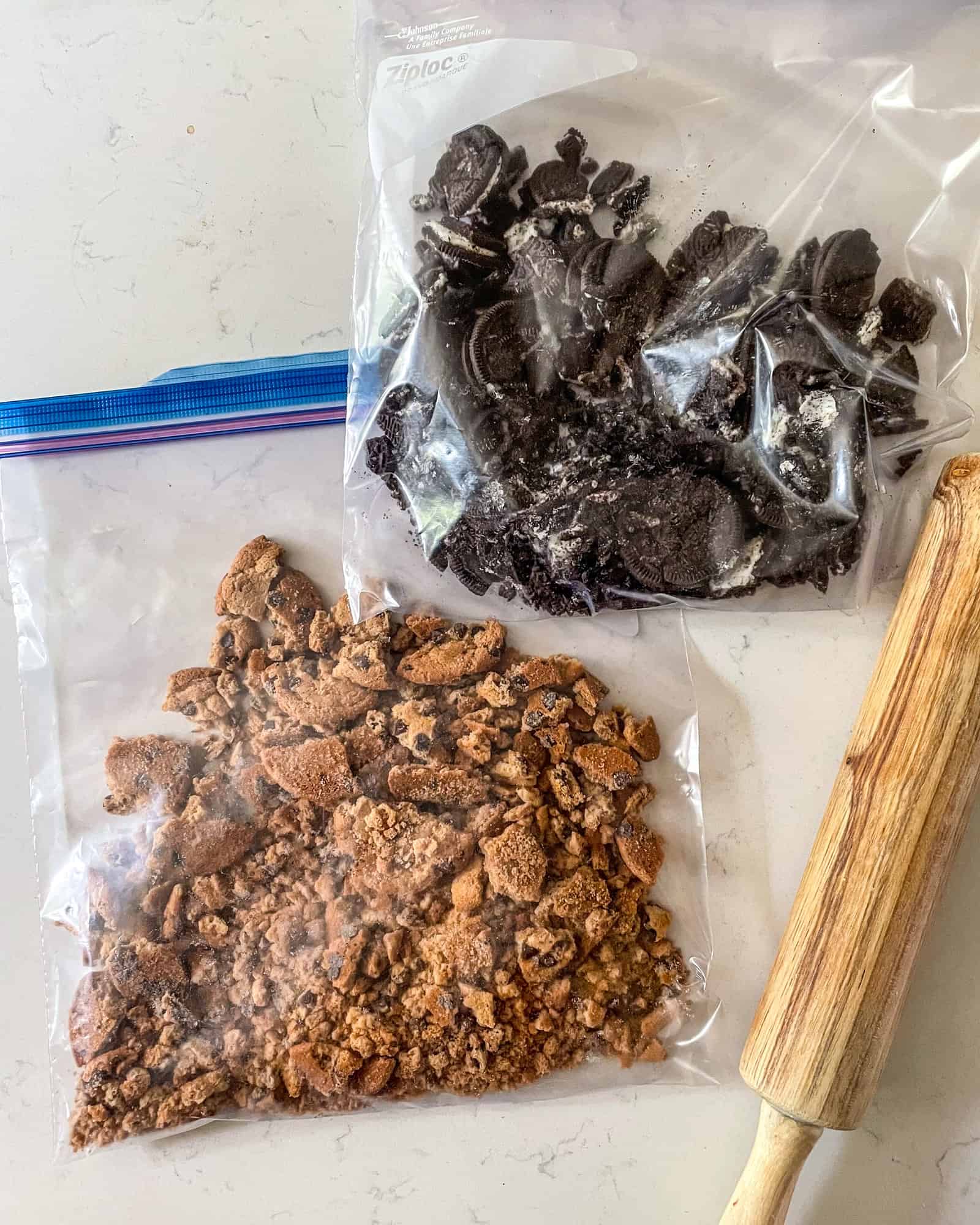 crushed oreos and chocolate chip cookies in a ziploc bag next to a dough roller.