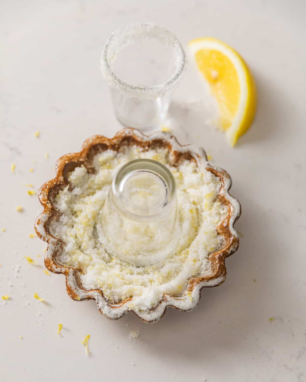 a shot glass being dipped into lemon sugar to create a sugar rim.