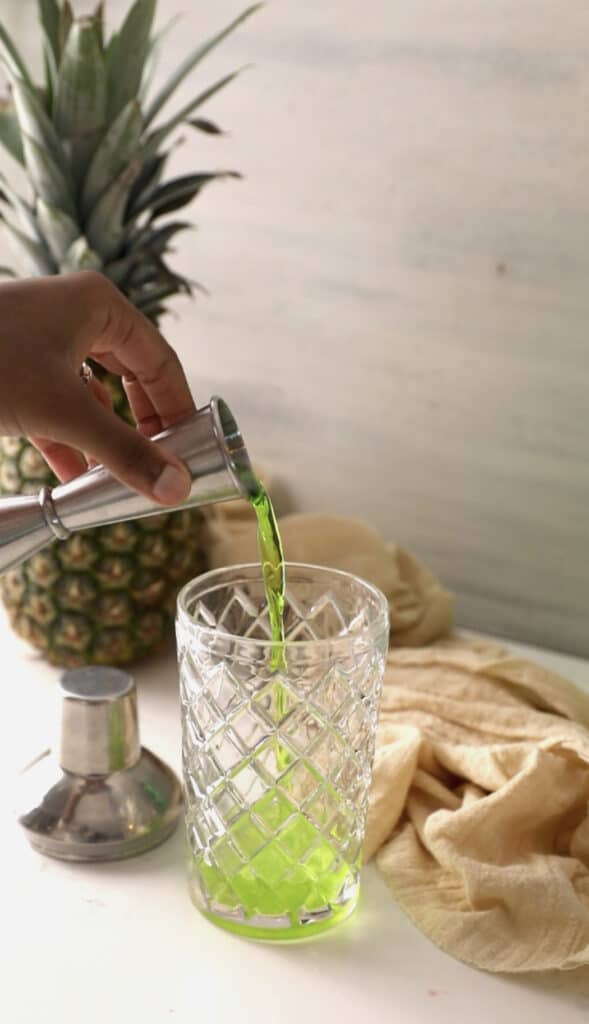 pouring melon liqueur into a cocktail shaker.