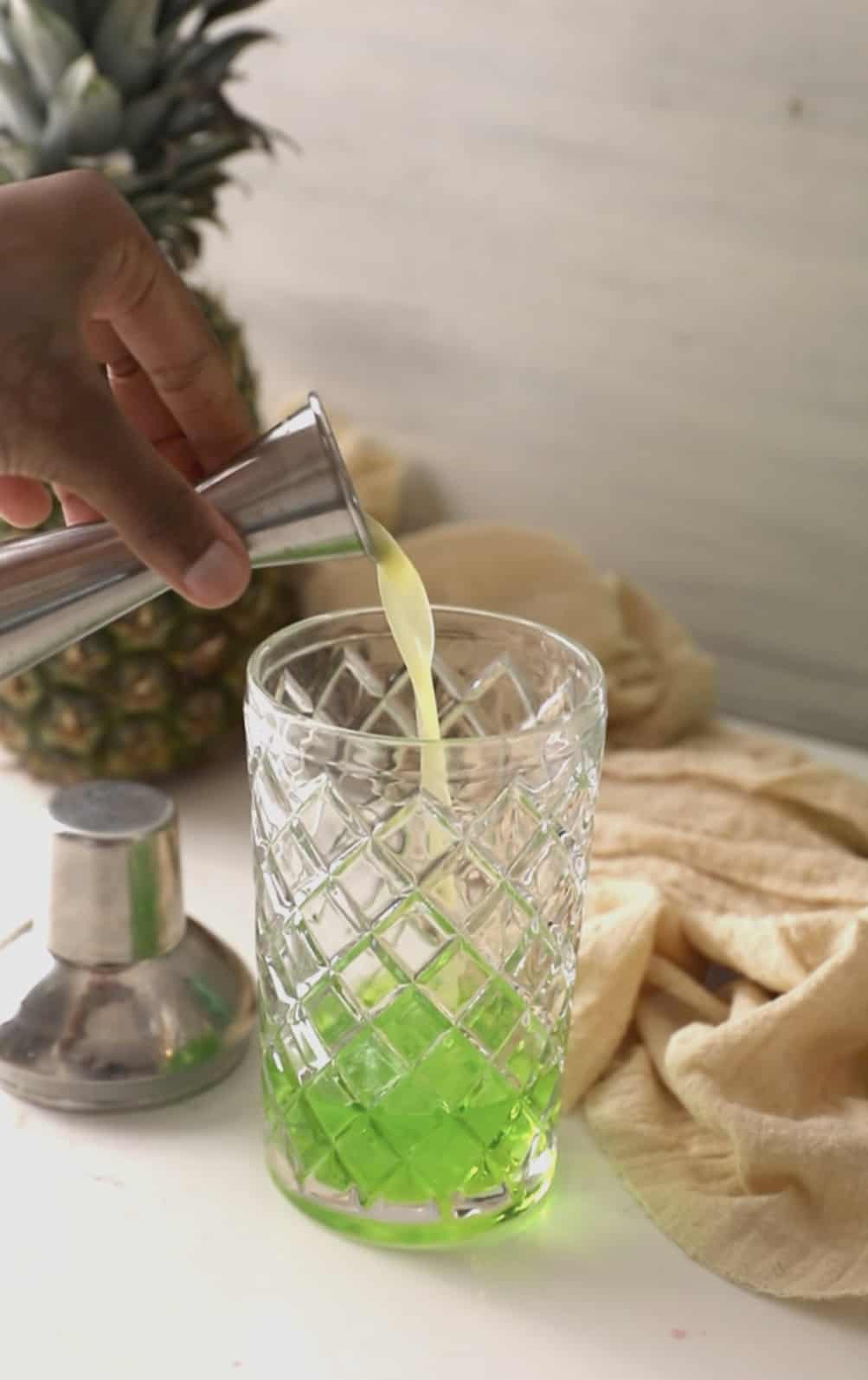 pouring pineapple juice into a cocktail shaker.