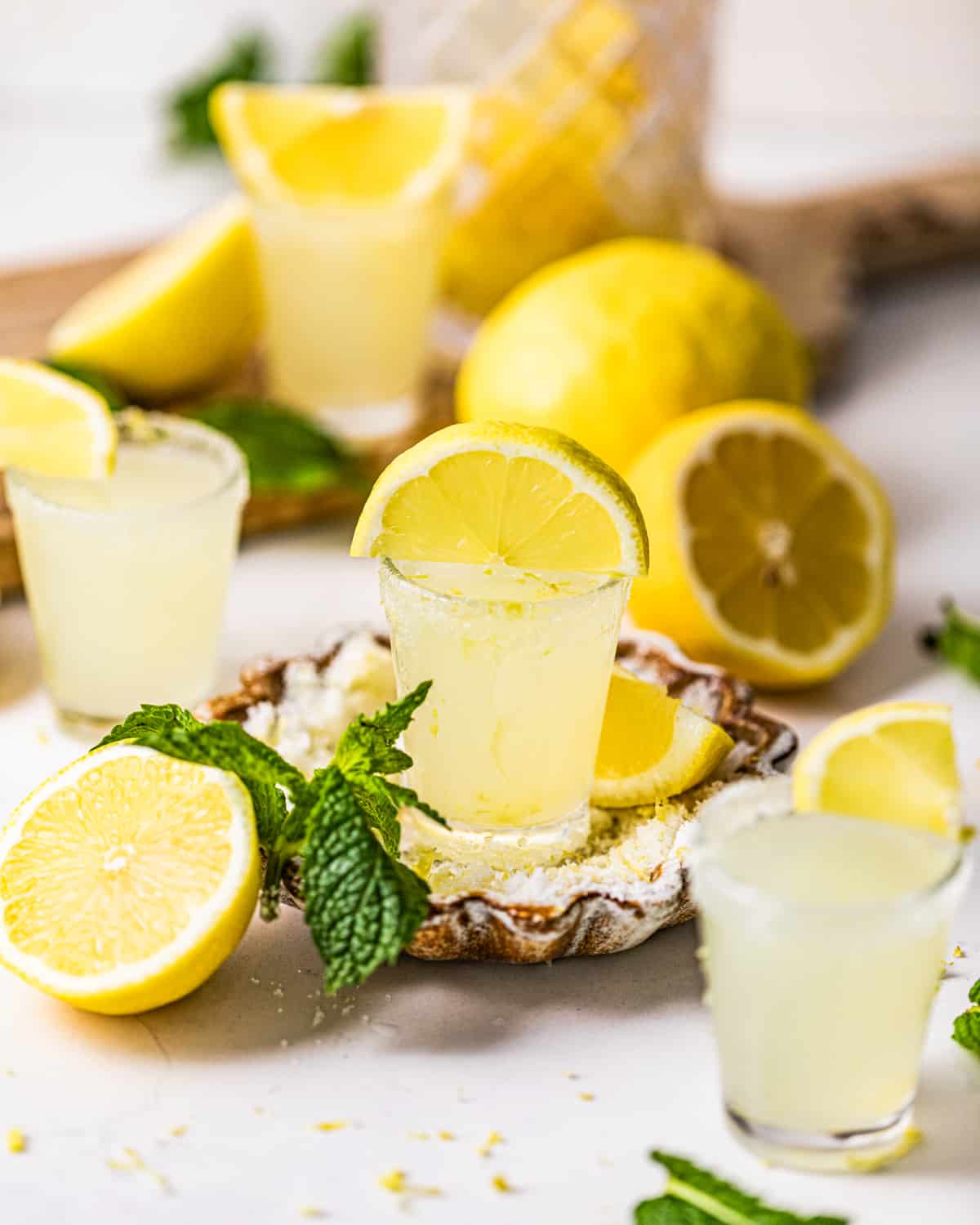 lemon drop shots surrounded by freshly cut lemons and garnished with mint leaves.