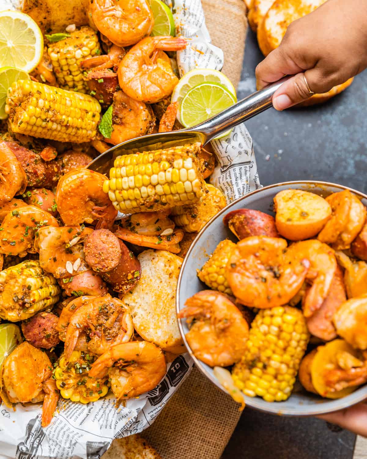 a hand scooping out seafood out of a low country boil and placing it into a bowl.