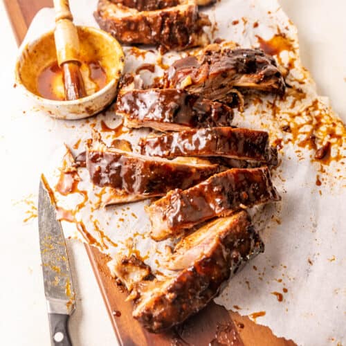 sliced rack of ribs on a brown serving board with a bowl of bbq sauce