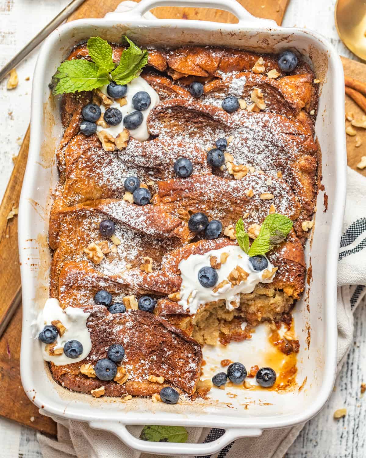 brioche french toast casserole in a baking dish topped with blueberries and whipped cream.