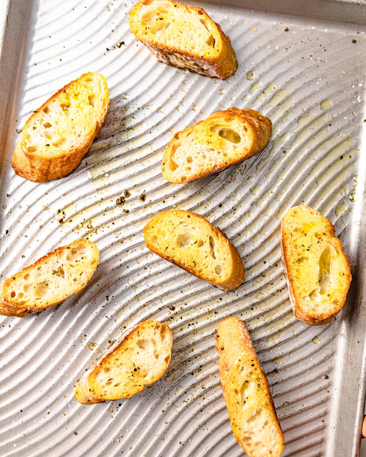 sliced bread on a baking sheet topped with olive oil, salt, and pepper.