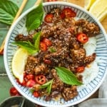 Crispy Chilli Beef in a bowl garnished with sesames seeds and fresh herbs.