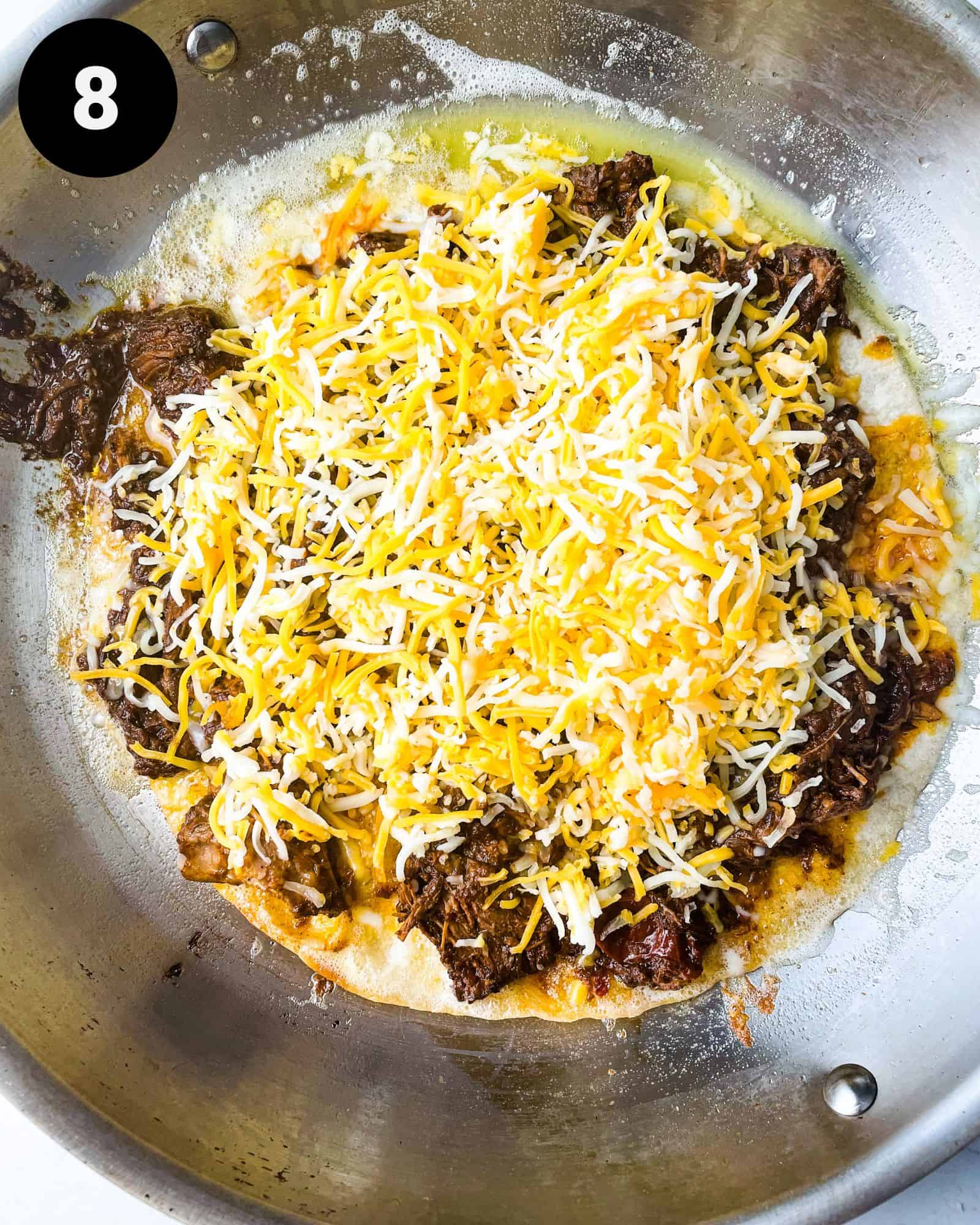 a tortilla in a pan topped with birria and cheese.