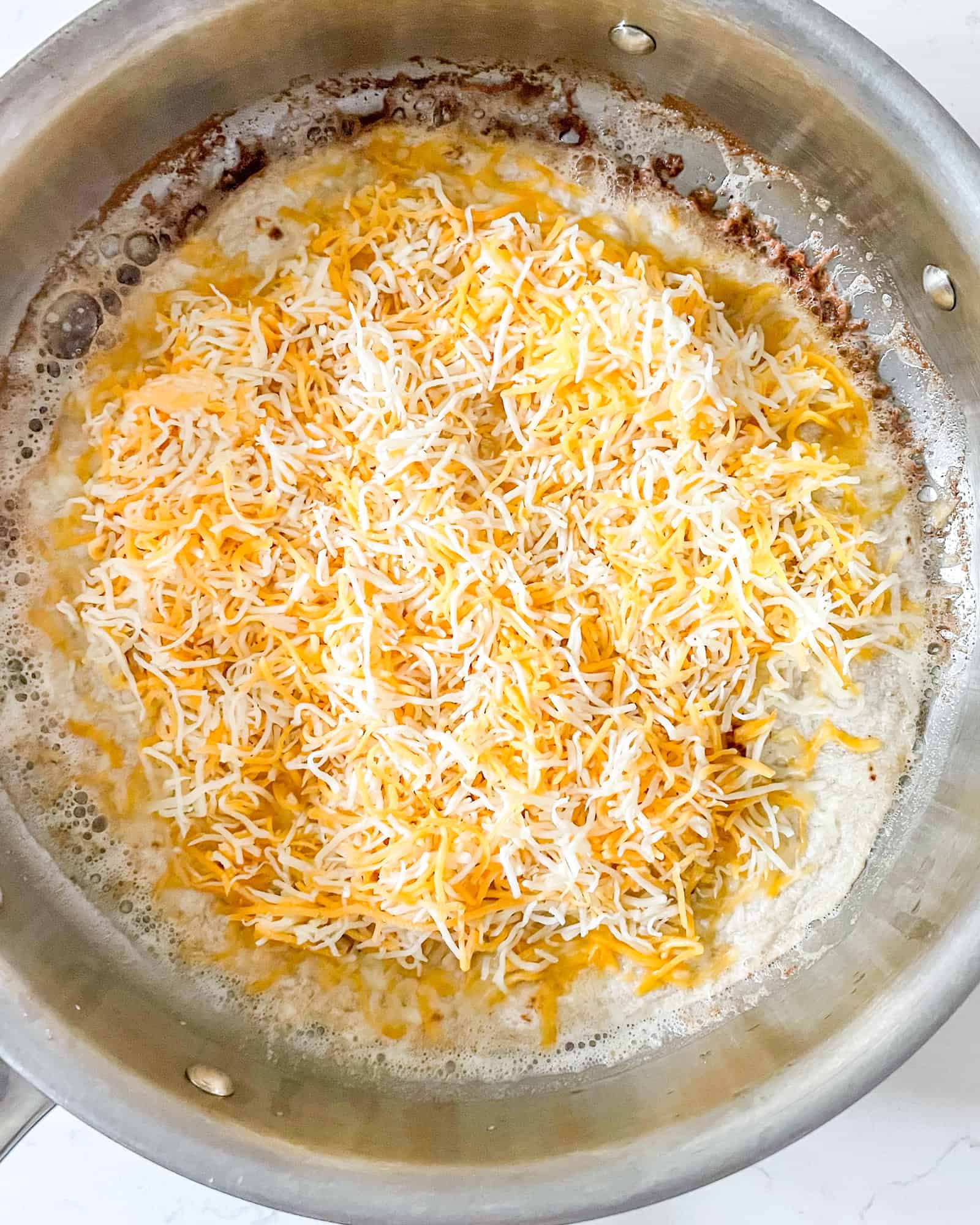 cheese on top of a flour tortilla in a frying pan.